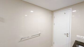 A bathroom with white tiles, a glass shower enclosure, a white door, and a towel rack.