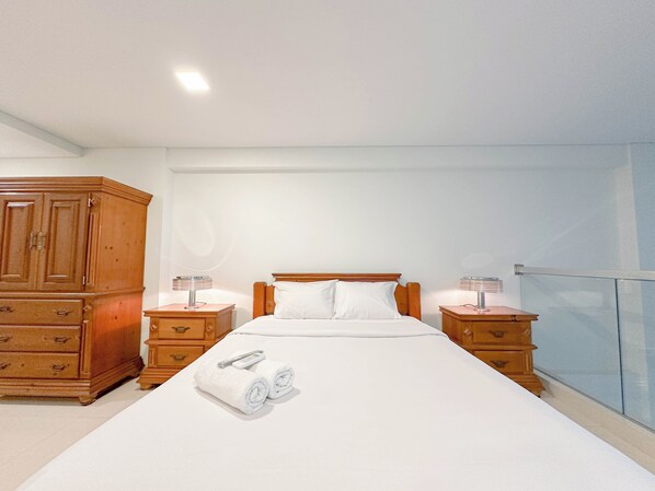 Habitación de hotel con una cama grande, dos mesitas de noche, un armario de madera y vistas al exterior.