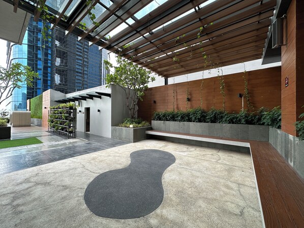 A modern outdoor area with a concrete floor, a wooden pergola, and a planter with greenery.