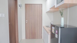 Une cuisine avec une porte en bois, un réfrigérateur en acier inoxydable, un four à micro-ondes et un vase blanc contenant des plantes.
