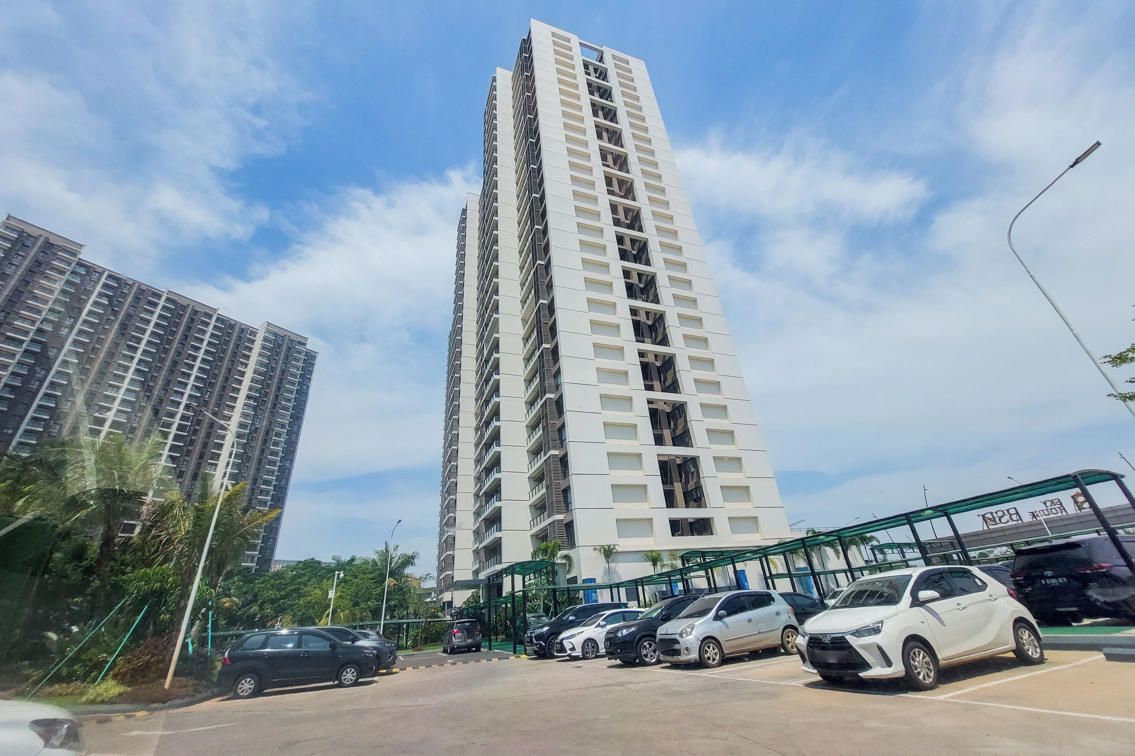 Um edifício residencial alto com vários andares, uma área de estacionamento com diversos carros e uma galeria coberta verde.