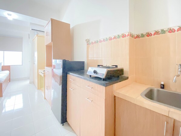 A kitchen with wooden cabinets, a countertop, a sink, and a stove. - Tranquil and Comfy Studio Apartment at Easton Park Residence Jatinangor (Cileunyi)