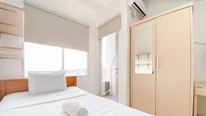 A hotel room with a bed, a wooden wardrobe, a window with a view, and an air conditioning unit.