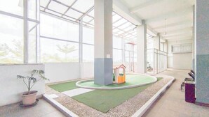 A spacious indoor area with large windows, a small play area with a green turf and a playhouse, and a potted plant.