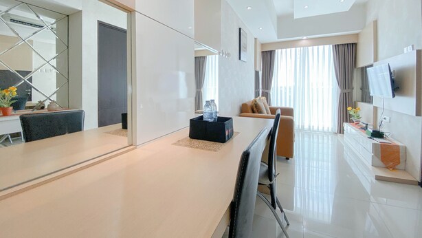 A modern hotel room with a large mirror, a dining area with a table and chairs, a sofa, a TV mounted on the wall, and a window with curtains.