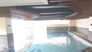 An indoor swimming pool with clear water, tiled floor, and a modern architectural design with a sloped ceiling and walls.
