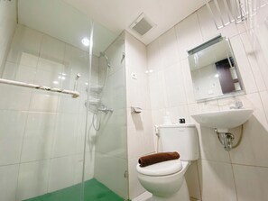 Un baño con ducha envuelta en vidrio, un inodoro blanco con una toalla marrón y un lavamanos instalado en la pared.