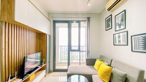 A modern living room with a flat-screen TV, a sofa with yellow cushions, a glass coffee table, and framed pictures on the wall. - Cozy and Spacious 2BR Apartment at Royal Olive Residence (Jakarta)