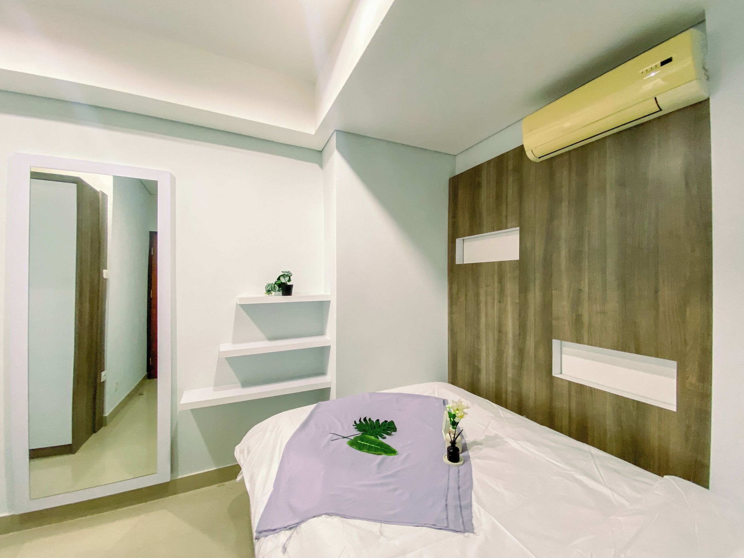 A hotel room with a bed, a mirror, a small plant, and a wooden wall panel.