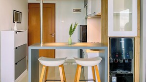 A modern kitchen with a double-height wooden ceiling, a built-in bar area with two stools, a refrigerator, and a water dispenser. - Cozy and Spacious 2BR Apartment at Royal Olive Residence (Jakarta)