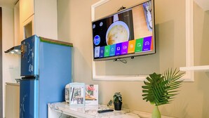 Ett modernt kök med ett blått kylskåp, en bänkskiva i marmor, en liten krukväxt och en väggmonterad tv som visar ett matlagningsprogram.