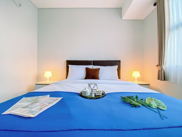 A hotel room with a large bed, two bedside lamps, a blue bedspread, a tray with toiletries, and a magazine on the bed. - Best and Cozy 2BR Apartment Royal Olive Residence (Jakarta)