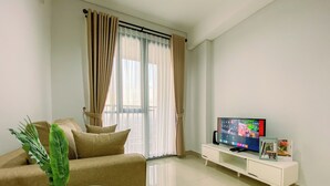 A living room with a sofa, a coffee table with a plant, a TV on a stand, and a window with curtains. - Best and Cozy 2BR Apartment Royal Olive Residence (Jakarta)