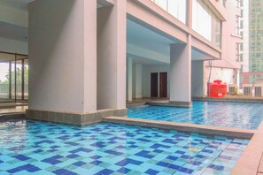 A swimming pool with blue and white tiles, surrounded by a building with large pillars and a balcony. - Best and Cozy 2BR Apartment Royal Olive Residence (Jakarta)
