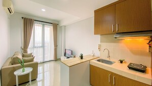 A modern kitchen with wooden cabinets, a stainless steel sink, and a countertop. There is a small island with a sink and a potted plant. The kitchen is adjacent to a living area with a sofa and a coffee table. - Best and Cozy 2BR Apartment Royal Olive Residence (Jakarta)