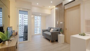 Un salon moderne avec un canapé gris, une porte en bois et un bureau blanc agrémenté d’une plante.