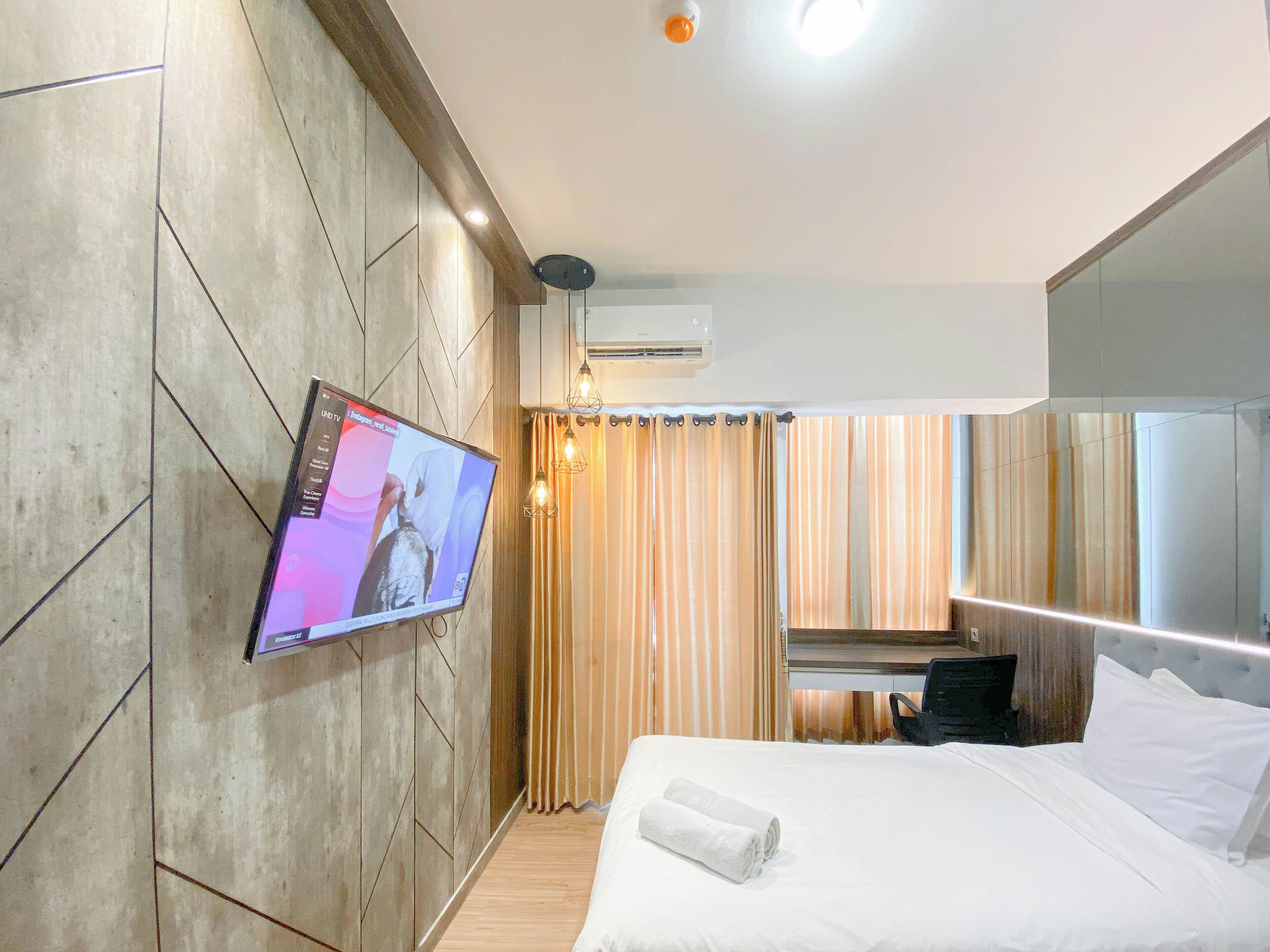 A hotel room with a bed, a TV mounted on the wall, a desk with a chair, and a large mirror.