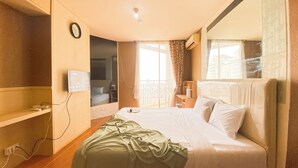 Ein Hotelzimmer mit Bett, Wandfernseher, Fenster mit Vorhängen und einem Balkon.