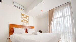 A hotel room with a large bed, a ceiling-mounted air conditioner, a wall-mounted artwork, and a window with sheer curtains. - The Spacious 2BR at Grand Asia Afrika Apartment (Bandung)