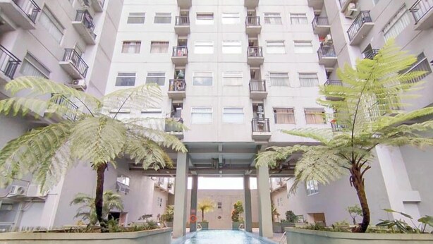 A modern apartment building with a central courtyard featuring a swimming pool, surrounded by large ferns and palm trees. - The Spacious 2BR at Grand Asia Afrika Apartment (Bandung)