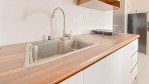 A kitchen with a stainless steel sink, wooden countertop, and white cabinetry. - The Spacious 2BR at Grand Asia Afrika Apartment (Bandung)