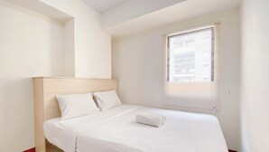 A neatly made bed with white linens, a wooden headboard, and a window with blinds.