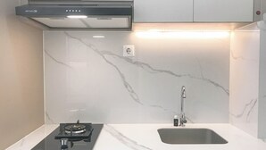 A modern kitchen with a built-in gas stove, a sink, and a stainless steel range hood. - Modern Studio at Bale Hinggil Apartment (Surabaya)