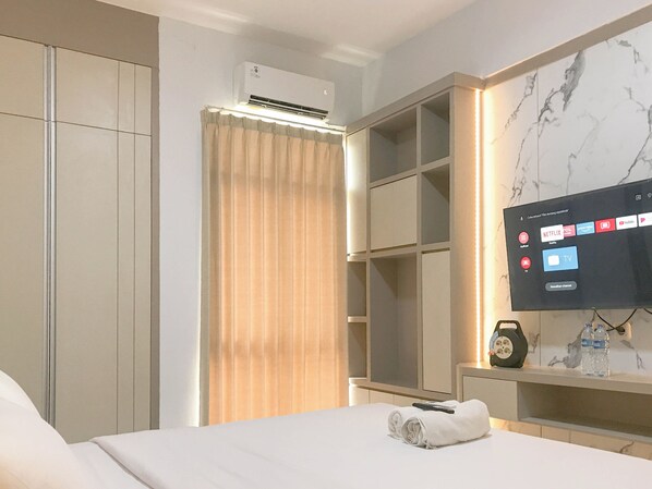 A hotel room with a bed, a TV mounted on the wall, a wardrobe, and an air conditioning unit. - Modern Studio at Bale Hinggil Apartment (Surabaya)
