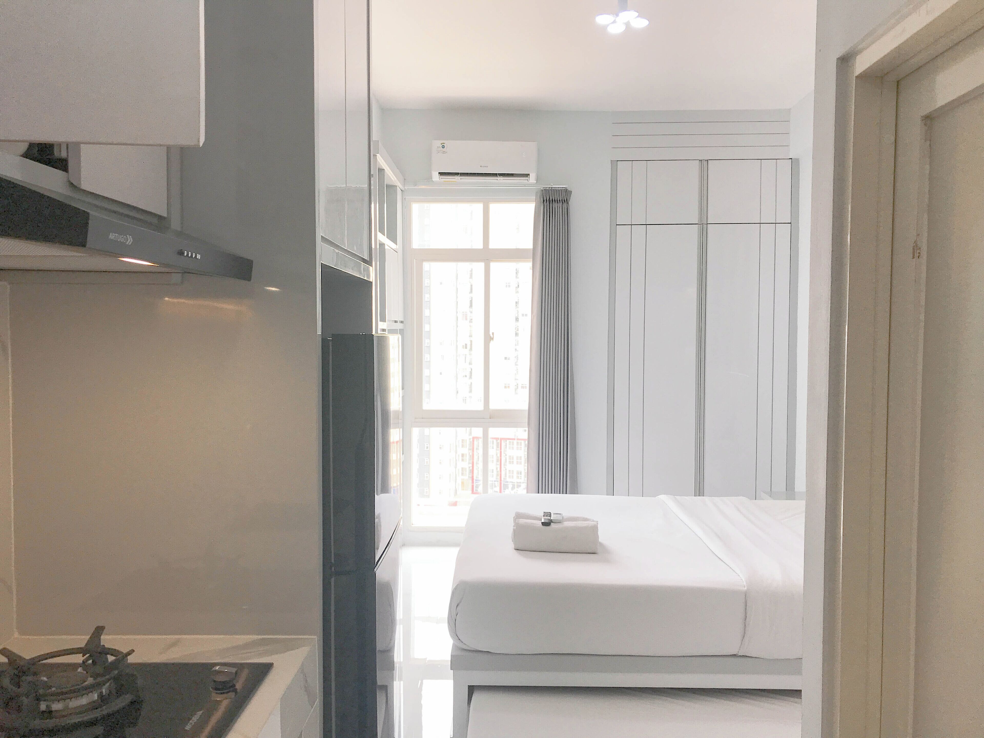 Una habitación de hotel moderna con una cama, un pequeño espacio de cocina con estufa y un ventanal con cortinas.