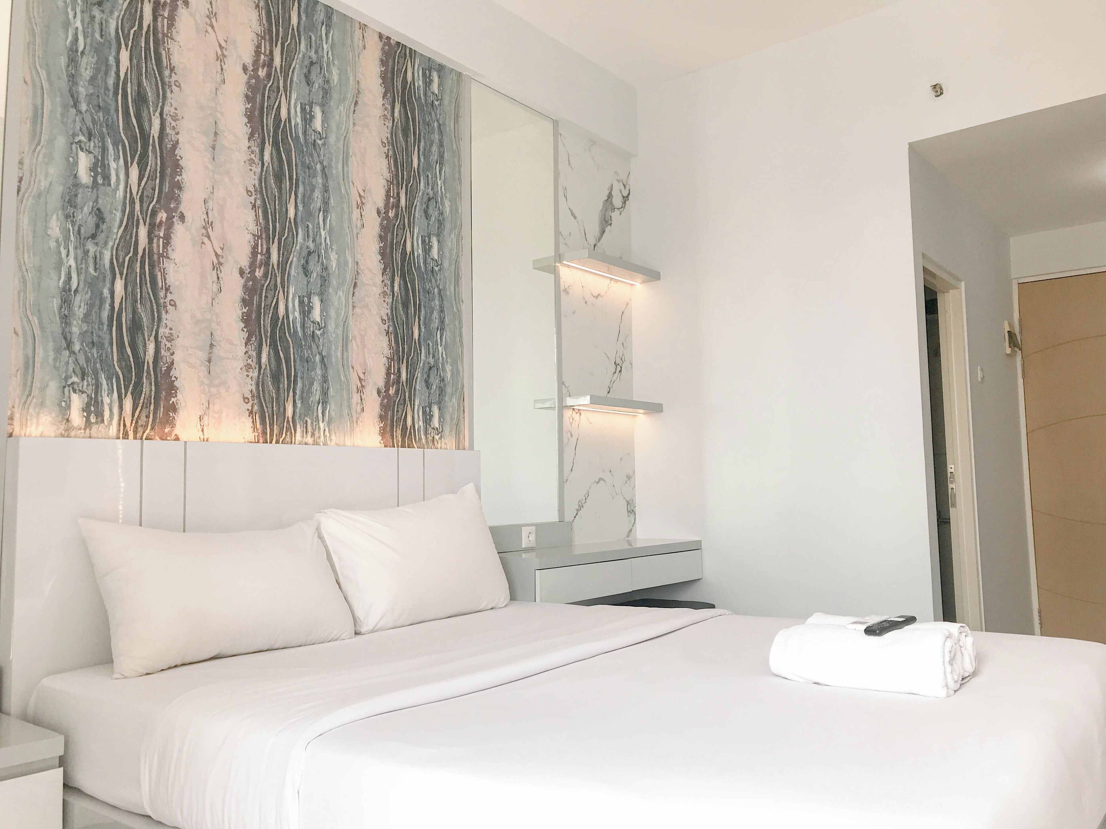 Une chambre d’hôtel moderne avec un grand lit, du linge de lit blanc, un mur décoratif en marbre et une table de chevet avec une télécommande.
