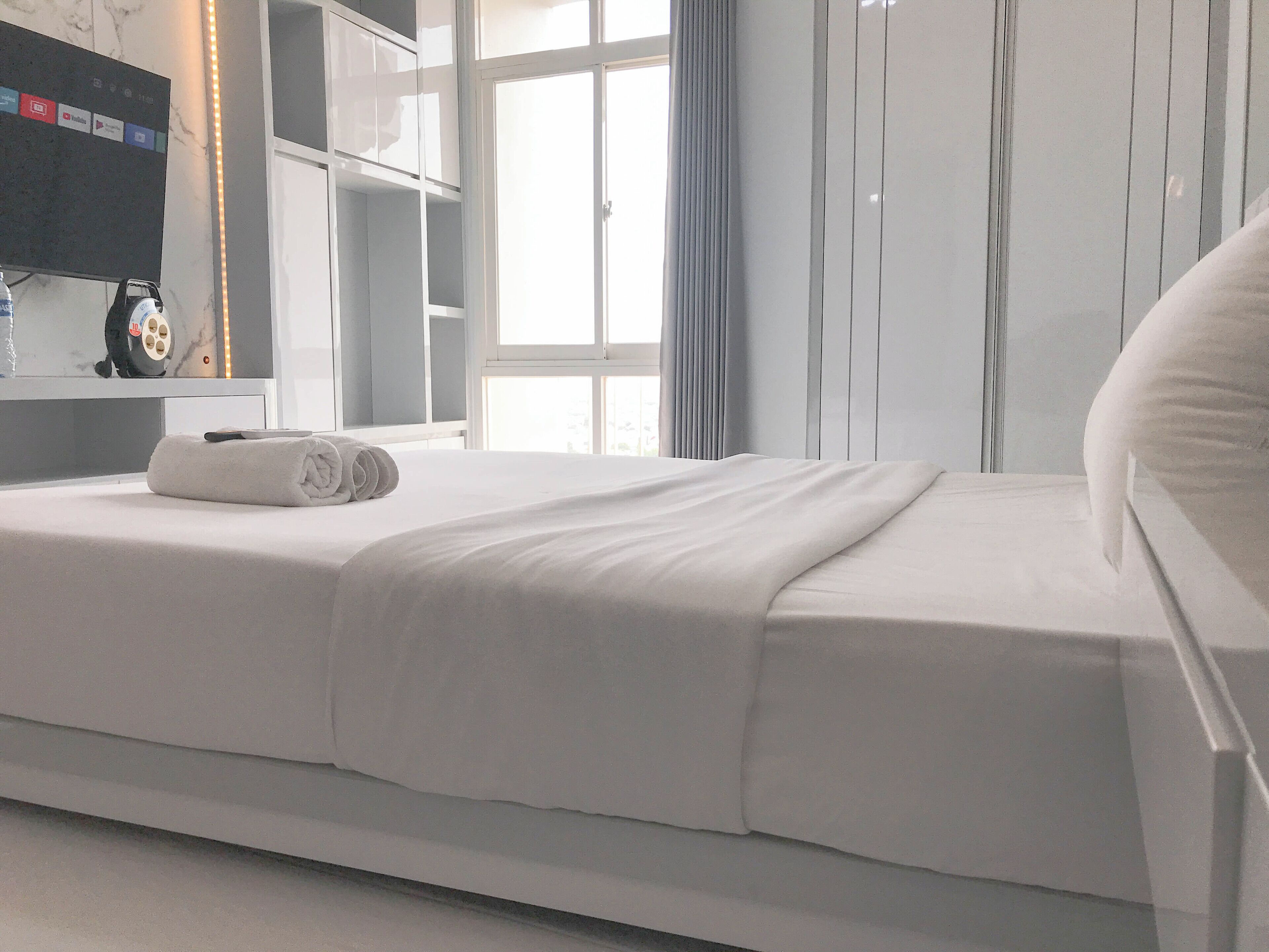 A modern hotel room with a neatly made bed, a flat-screen TV mounted on the wall, and a large window with curtains.