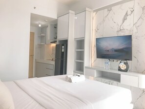 A hotel room with a bed, a television mounted on the wall, a minibar, and a marble-patterned wall. - Wonderful Studio at Bale Hinggil Apartment (Surabaya)