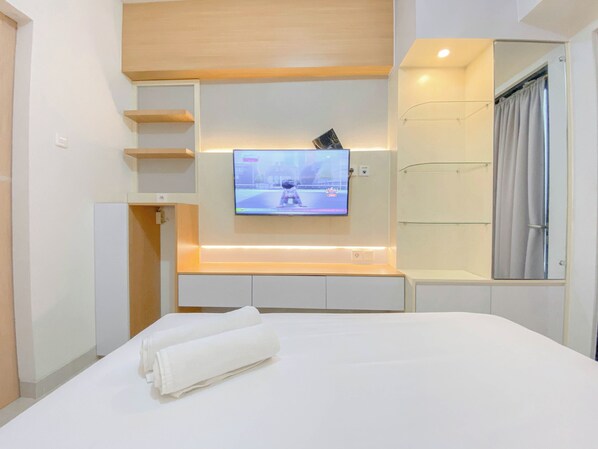 Een moderne hotelkamer met een flatscreen televisie aan de muur, een opgemaakt bed met witte lakens en een douchecabine van glas.