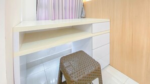 Ein Zimmer mit weißem Schreibtisch, Schubladen, einem Korbstuhl und einem Vorhang.