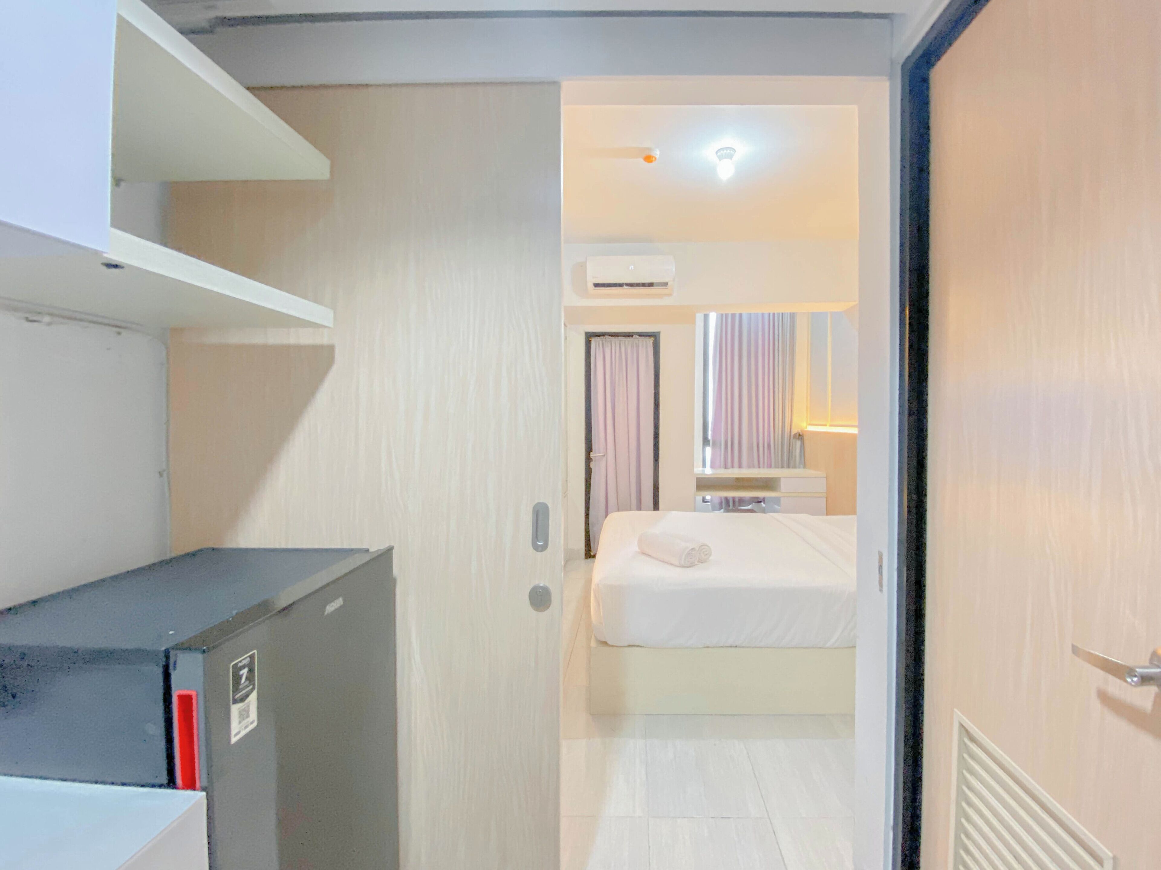 A compact hotel room with a bed, a small bedside table, a mirror, and an air conditioning unit.