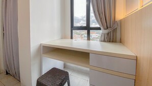 Ein Zimmer mit Schreibtisch, kleinem Hocker und einem Fenster mit Vorhängen.