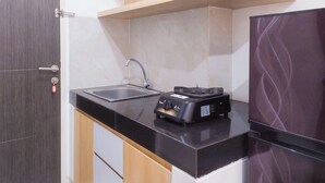 Una cocina compacta con encimera negra, un lavamanos y un refrigerador pequeño.