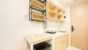 A compact kitchen with a white countertop, a sink, and a black trash bin. There is a wall-mounted shelf above the countertop and a door to the right. - Cozy Living and Homey Studio at Apartment Tokyo Riverside PIK 2 (Teluknaga)