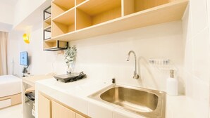 A modern kitchen with a stainless steel sink, white cabinets, and a built-in shelf above the counter. - Cozy Living and Homey Studio at Apartment Tokyo Riverside PIK 2 (Teluknaga)