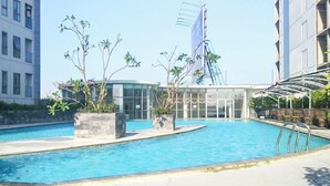 Une piscine dotée d’une enceinte en verre, entourée de plantes en pot et bordée d’un bâtiment moderne sur lequel flotte un drapeau.