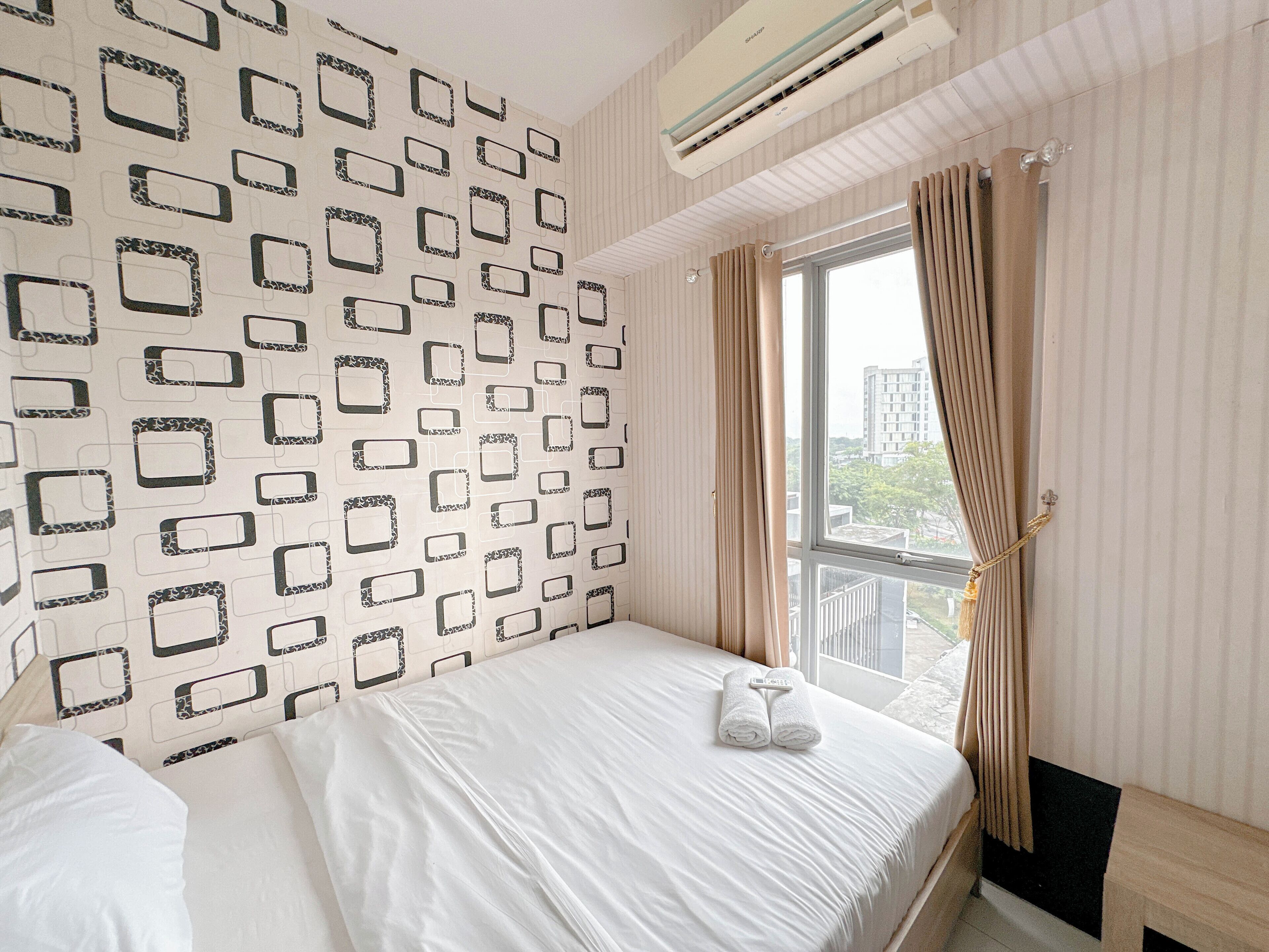 Hotellihuone, jossa on kuvioitu seinä, valkoisilla lakanoilla varustettu sänky, verhoilla varustettu ikkuna ja ilmastointilaite.