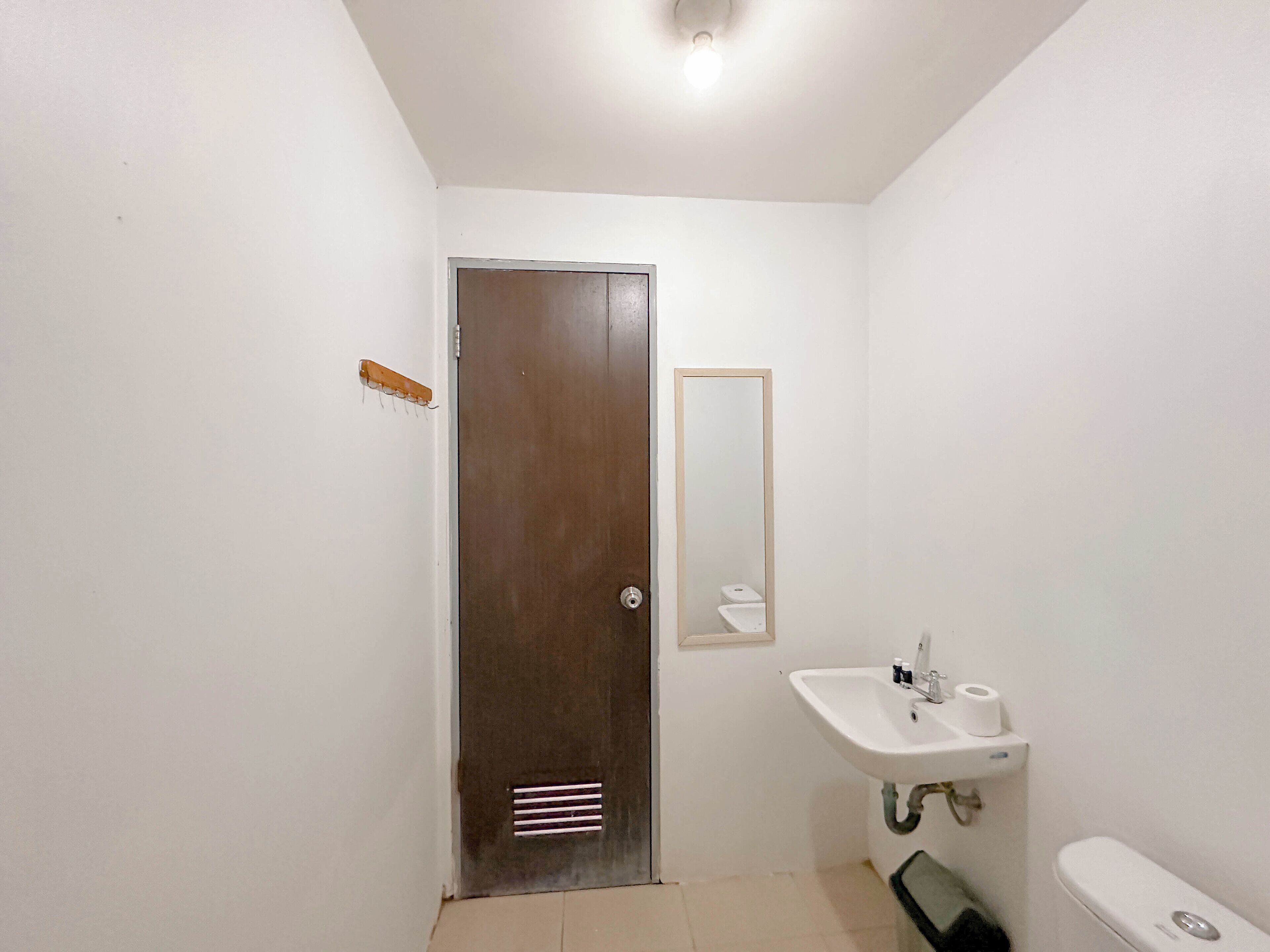 A small, clean bathroom with a white sink, toilet, and a door with a metal handle.