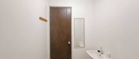 A small, clean bathroom with a white sink, toilet, and a door with a metal handle.