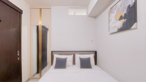 A bedroom with a bed, two pillows, a wooden headboard, a painting on the wall, and a door.