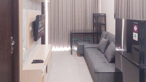 A modern living room with a sofa, a TV mounted on the wall, a refrigerator, and a dining table with chairs.