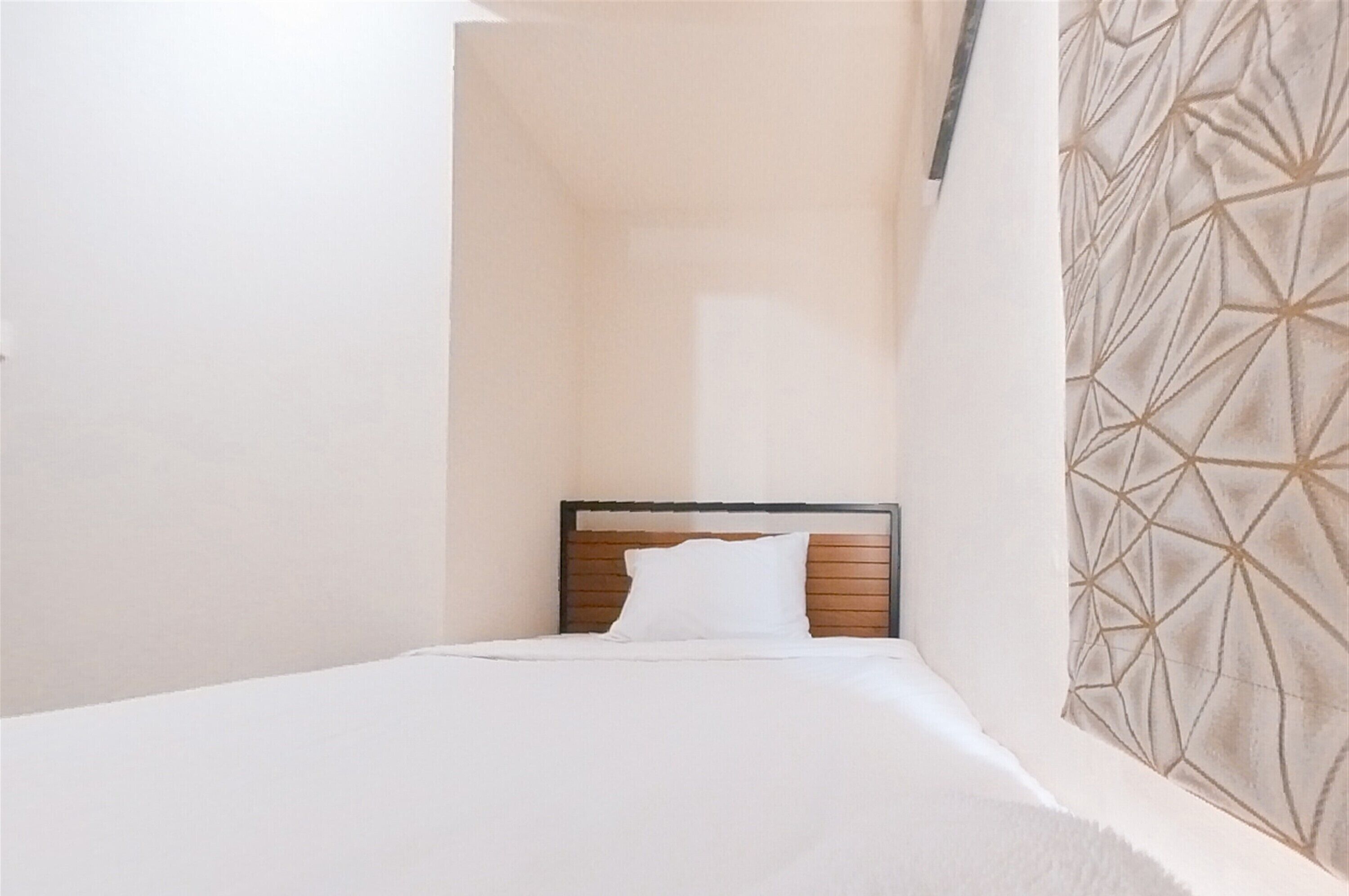 A small, neatly made bed in a corner room with a simple wooden headboard and a plain wall on one side.