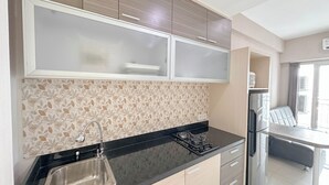 Una cocina moderna con encimera negra, pileta de acero inoxidable y estufa a gas. Se observan muebles de madera con una sección superior de vidrio. Se ve un refrigerador al fondo.