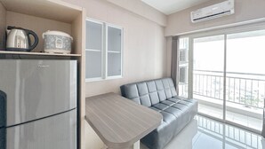Una cocina moderna con un refrigerador, una cafetera y un hervidor sobre la encimera. Hay un sofá gris y una mesita en la sala.