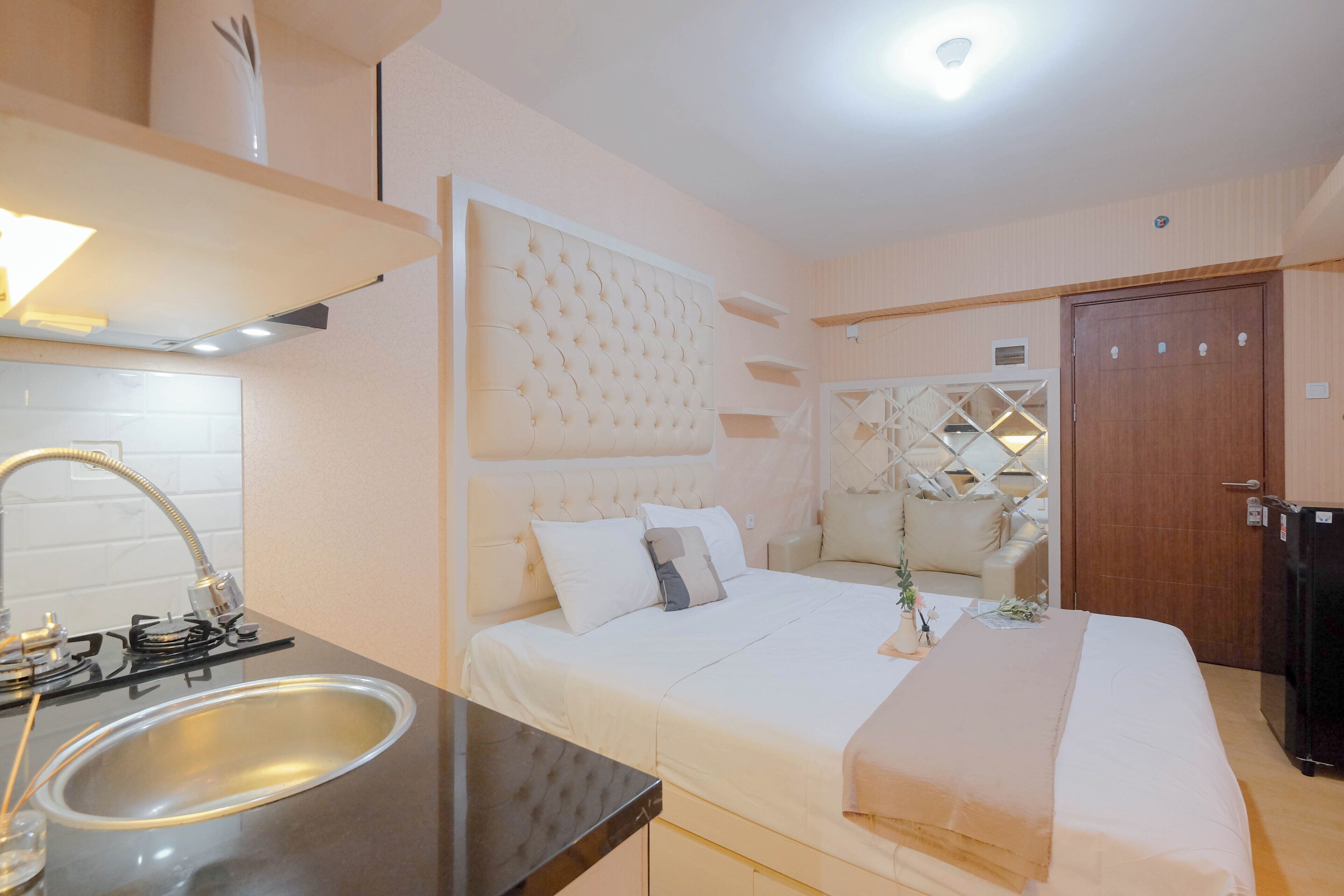 A hotel room with a bed, a built-in sink, a wooden door, and a small kitchen area.
