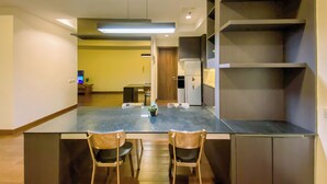A modern kitchen with a dark countertop, two wooden chairs, and a built-in refrigerator. - Spacious and Cozy 2BR Apartment Kemang Village (Jakarta)